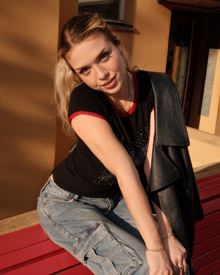 Woman sitting on a red bench wearing a black crop top with diamonds (rhinestones) and blue jeans.