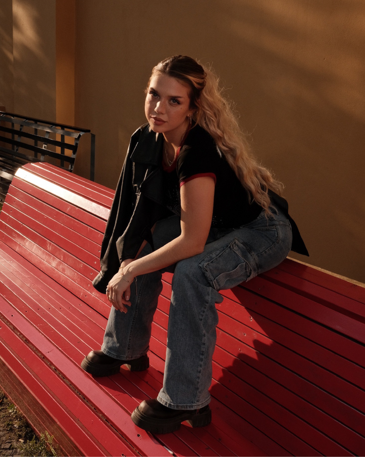 Woman sitting on a red bench wearing a black crop top with diamonds and rhinestones, and blue jeans.