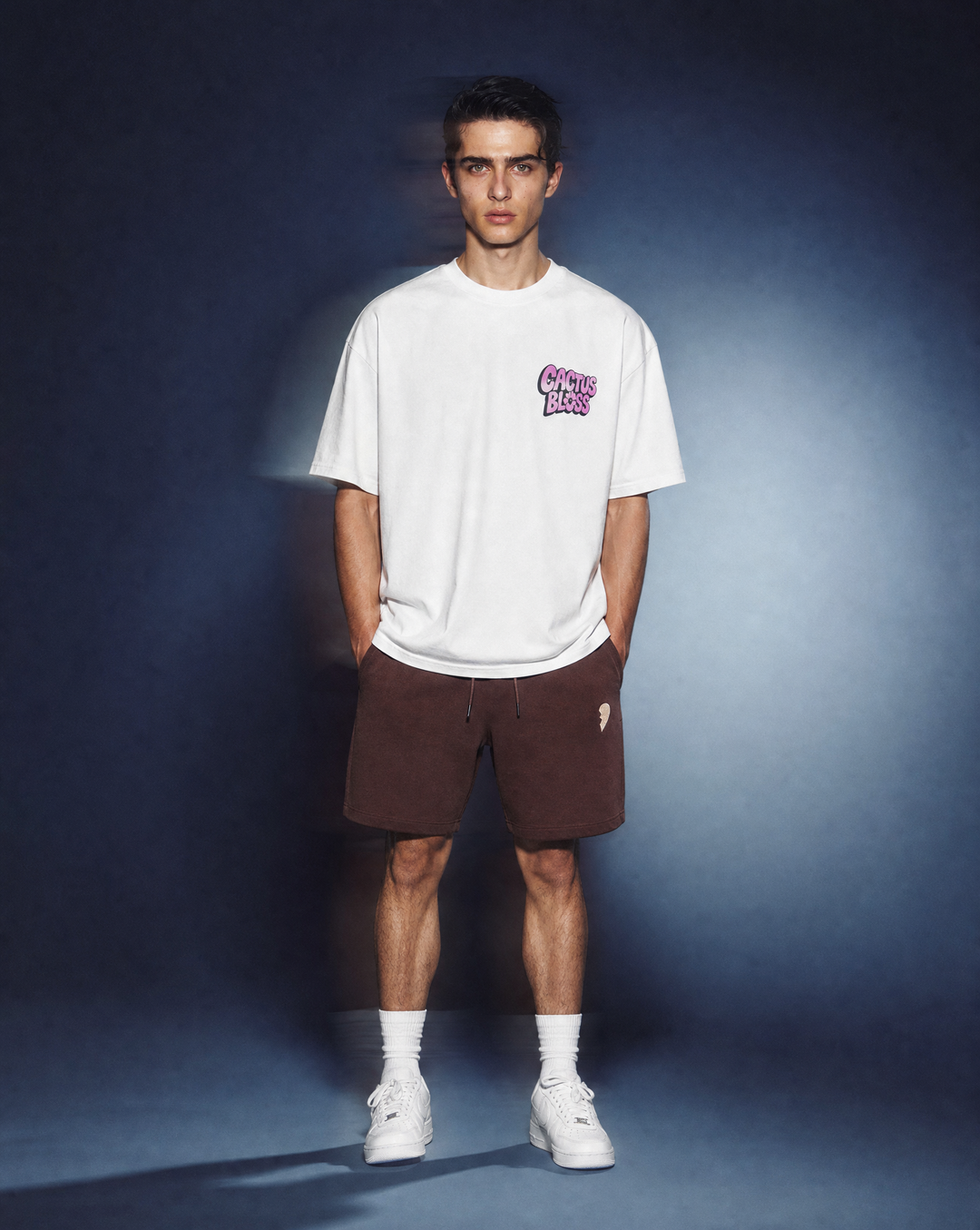 Person wearing a daisy flower t-shirt by Cactus Becks and a brown Cactus Becks shorts with a broken heart logo, against a blue background