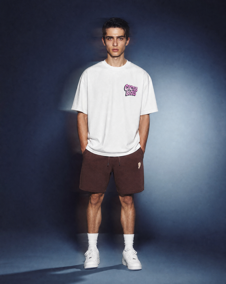 Person wearing a daisy flower t-shirt by Cactus Becks and a brown Cactus Becks shorts with a broken heart logo, against a blue background