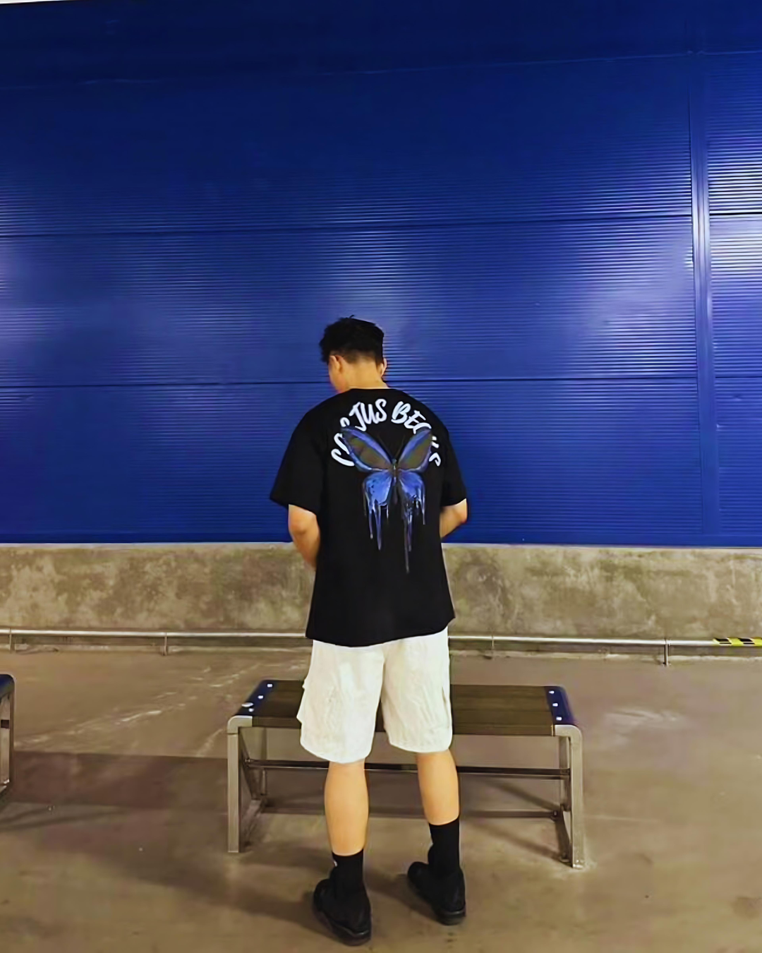 Person wearing a black t-shirt with a blue graphic design standing in front of a blue garage door.