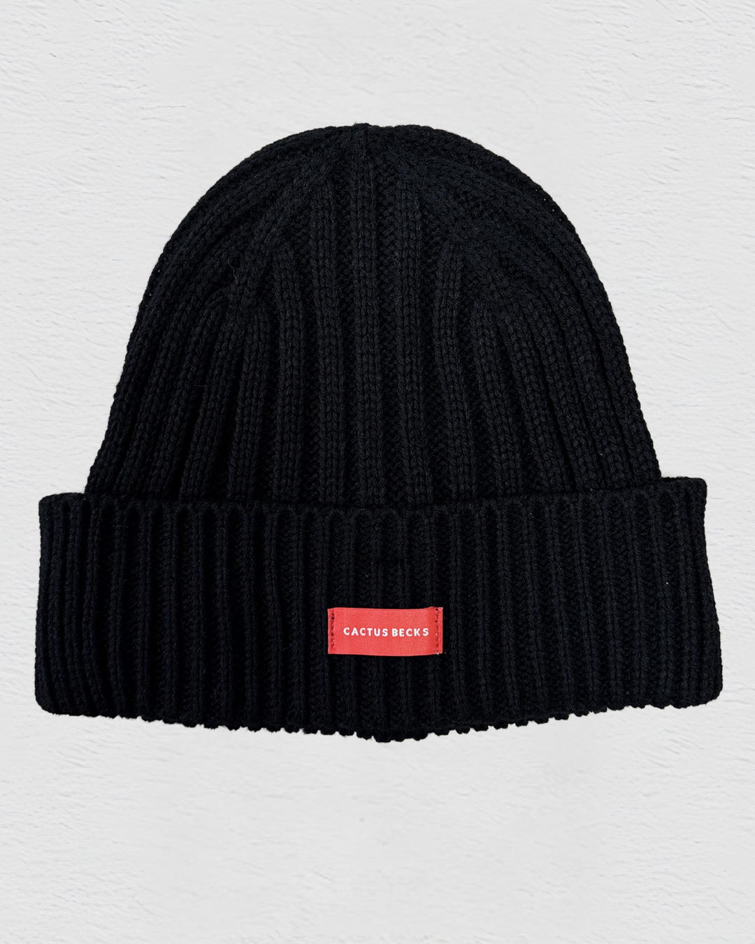 Black beanie with a red label on a light gray background