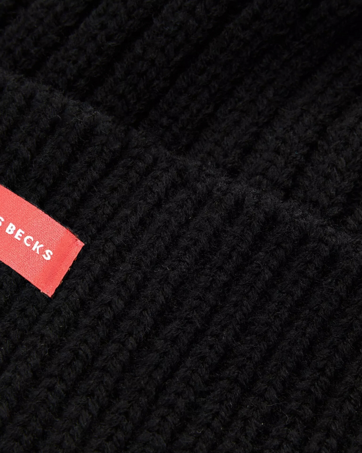 Close-up of a black knit fabric with a red label featuring 'CACTUS BECKS' branding.