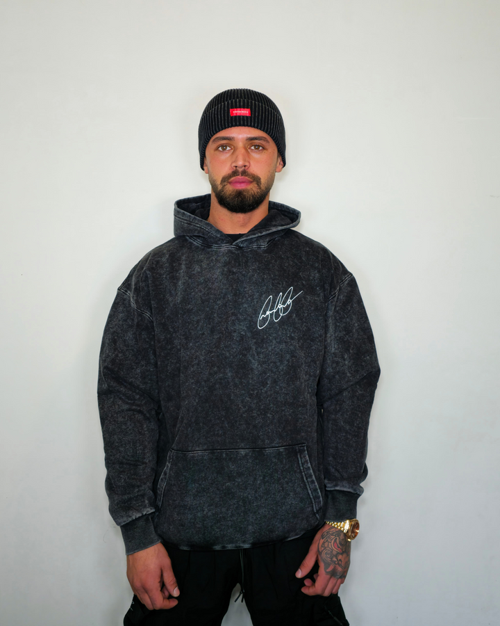 Man wearing a black hoodie with a logo and a beanie against a white background