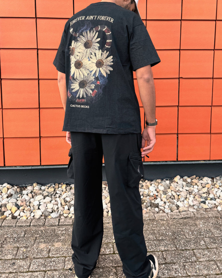 Person wearing a black t-shirt with floral design and text, standing against an orange tiled wall.