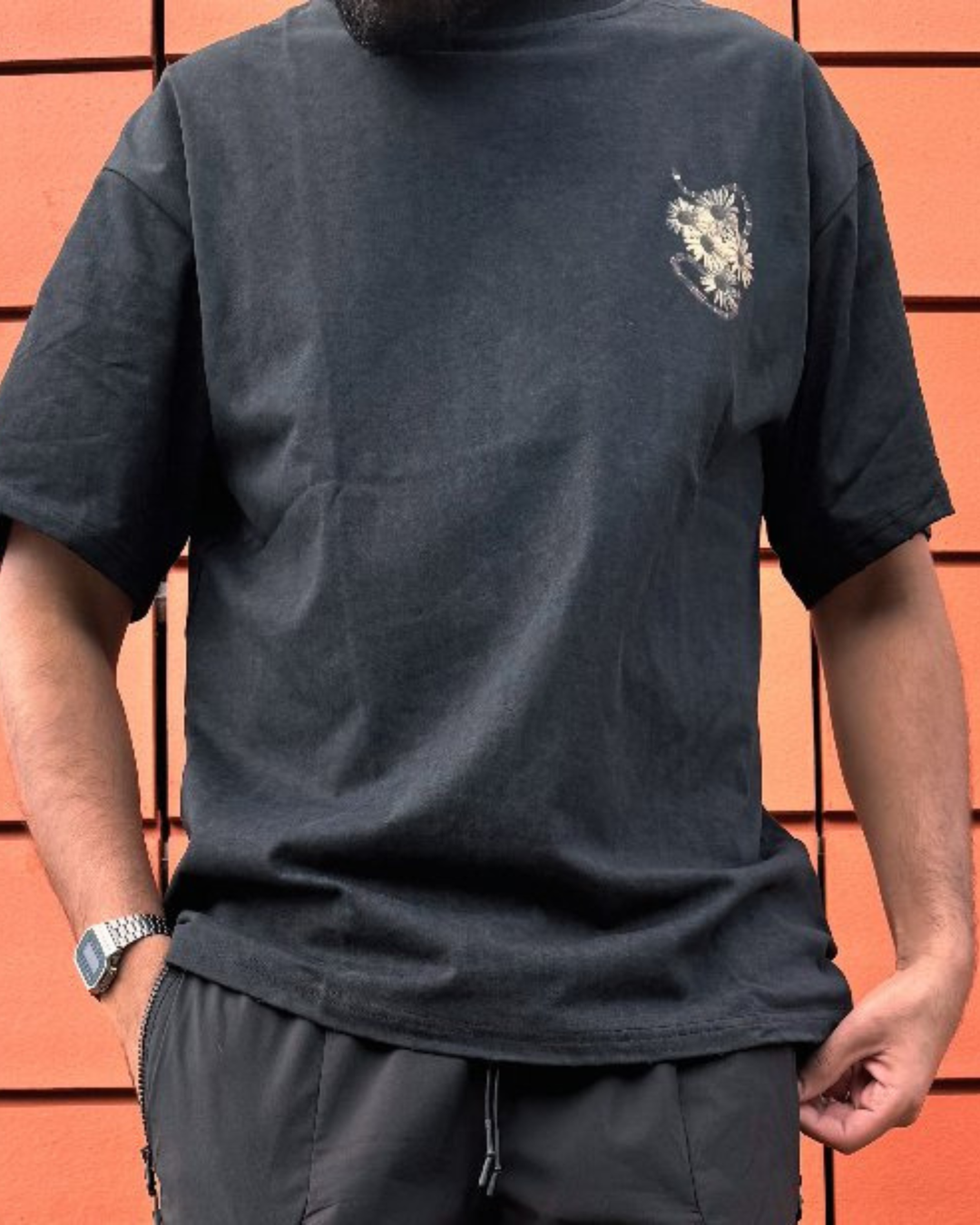 Person wearing a black t-shirt with a small design on the chest against an orange wall.