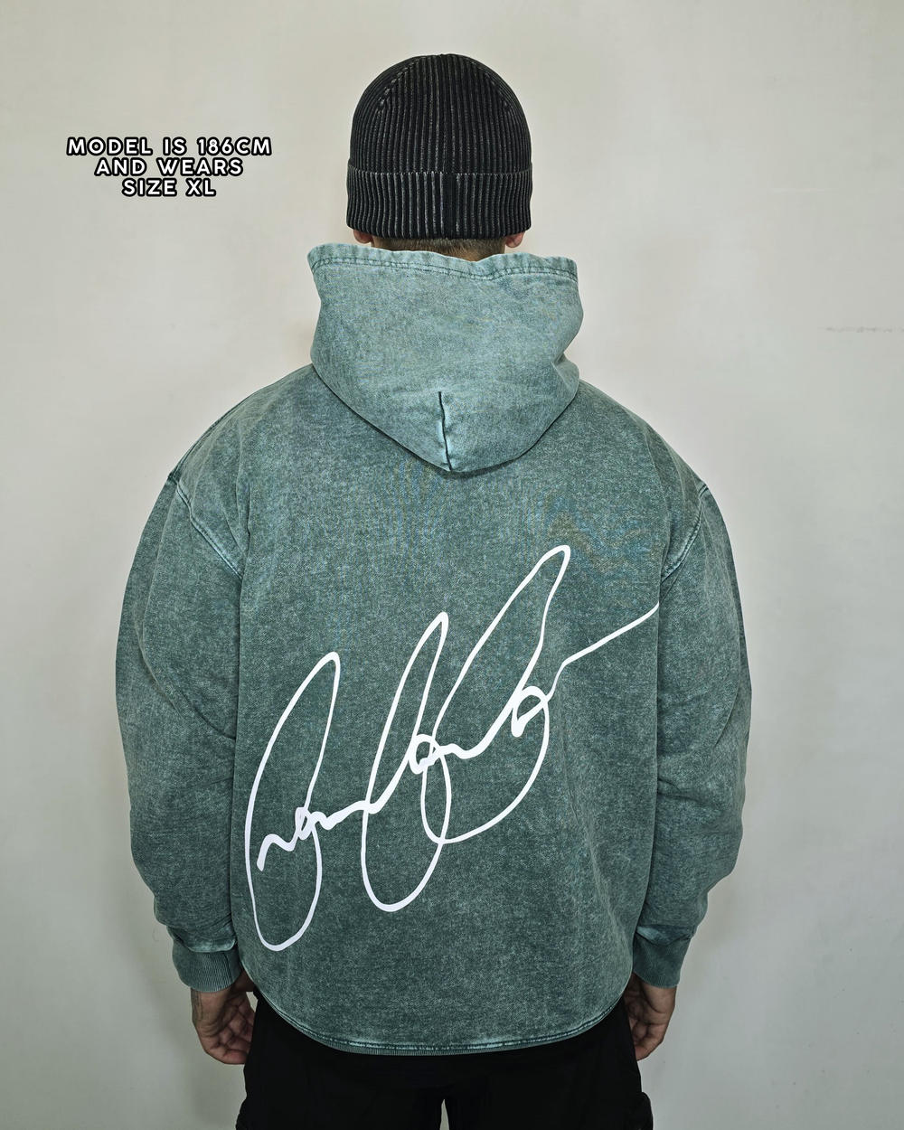 Person wearing a green hoodie with a signature design on the back, standing against a plain background.