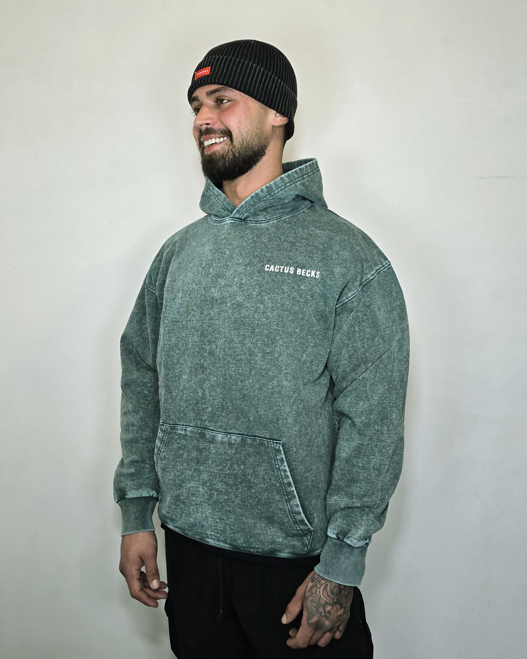 Man wearing a green hoodie with text and a black beanie against a plain background