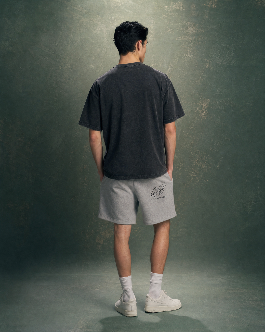 Person wearing a black t-shirt with a horse and burned house design and text, and a grey shorts, standing against a plain background