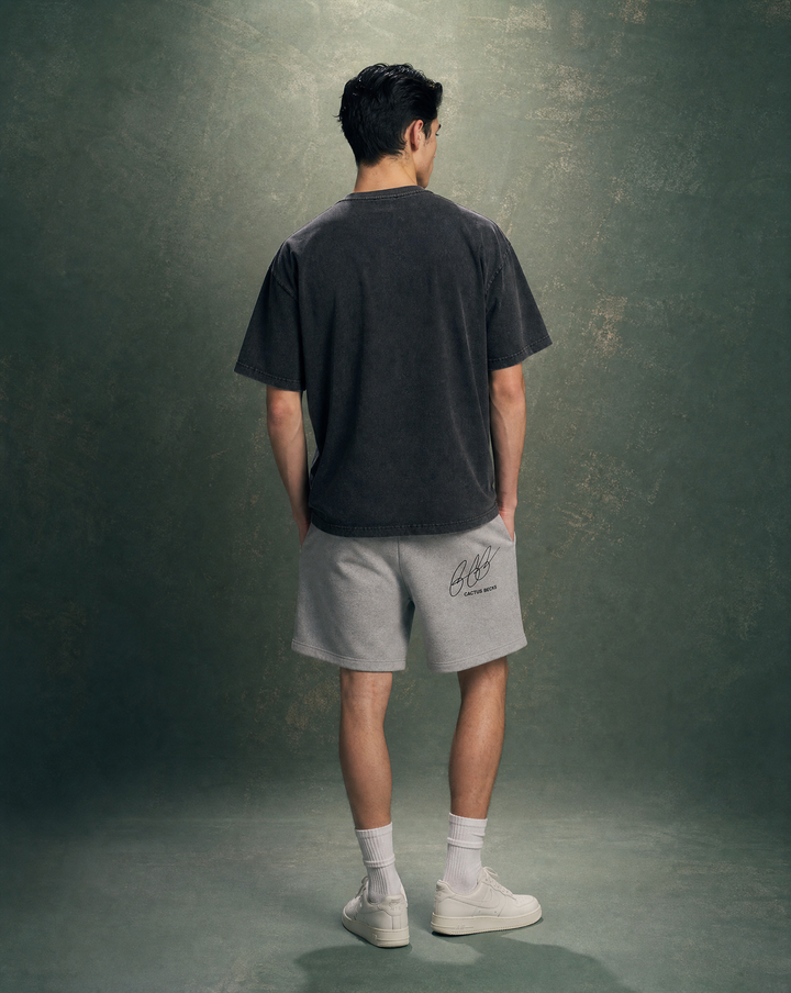 Person wearing a black t-shirt with a horse and burned house design and text, and a grey shorts, standing against a plain background