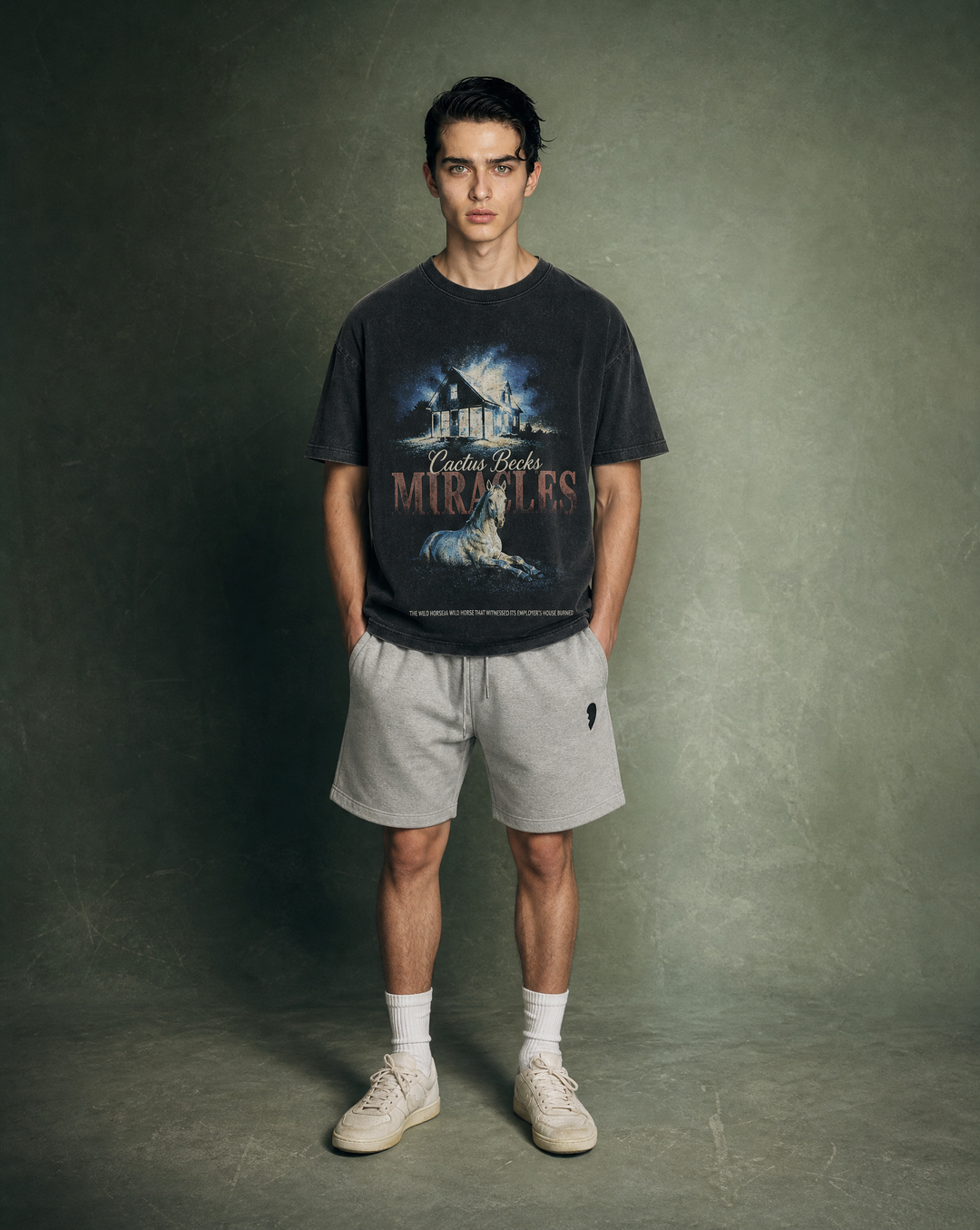 Person wearing a black t-shirt with a horse and burned house design and text, and a grey shorts, standing against a plain background.