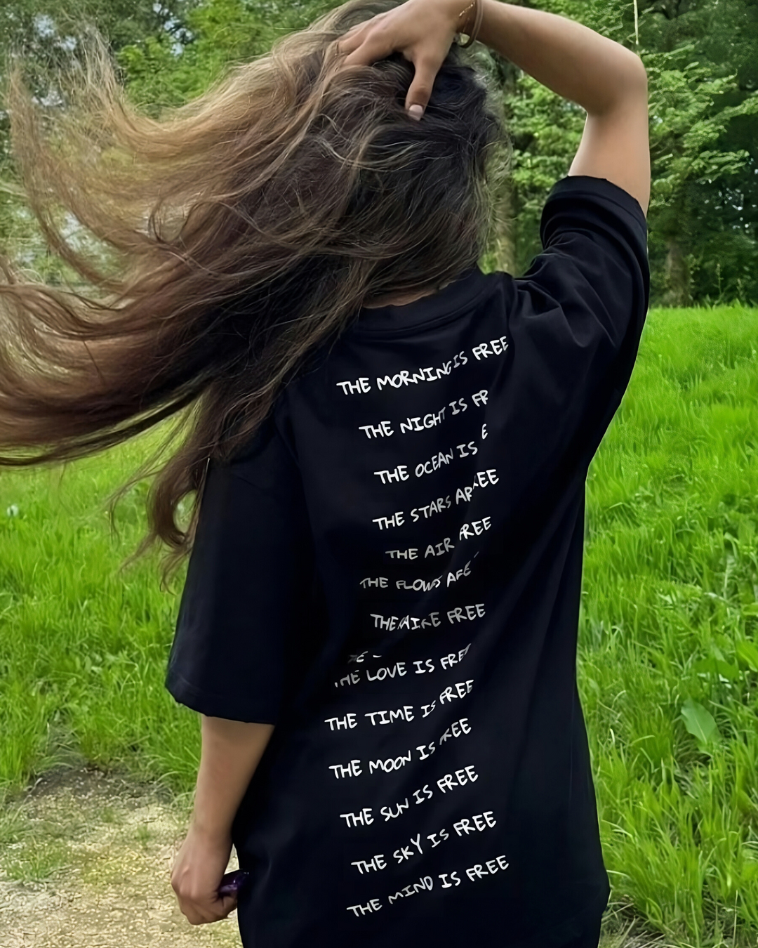 Person wearing a black t-shirt with text on the back, standing in a grassy field.