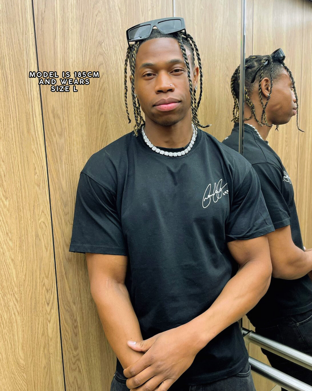 Person wearing a black t-shirt with a logo in front of a wooden wall.
