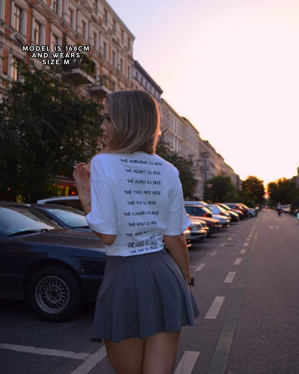 Woman walking on a street wearing a white t-shirt with text on the back.