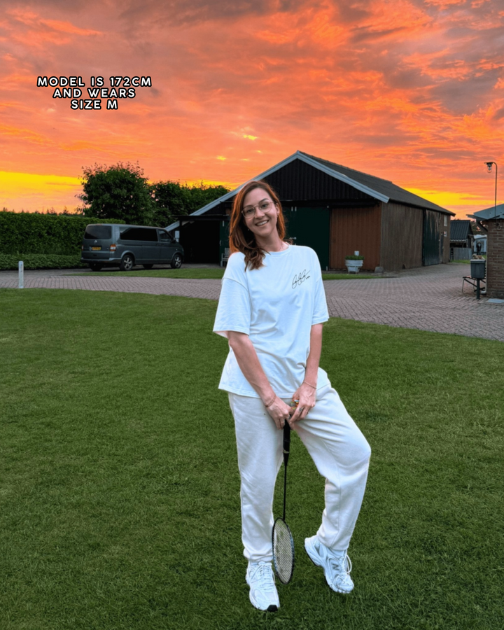 Person in white outfit holding a tennis racket on grass with sunset sky