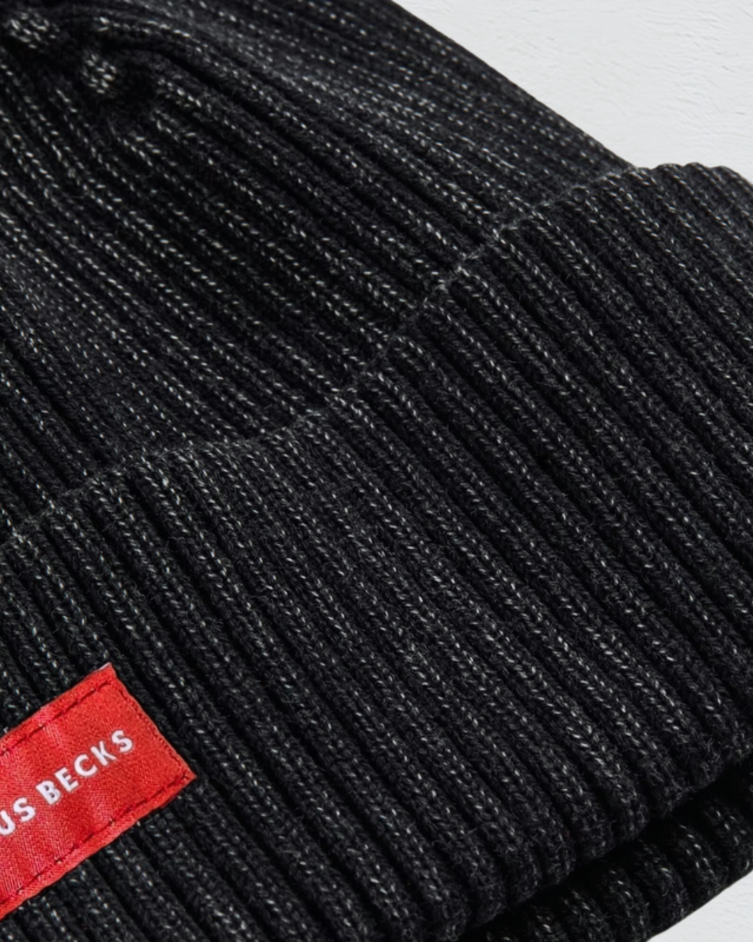 Close-up of a black ribbed knit beanie with a red label on a white background